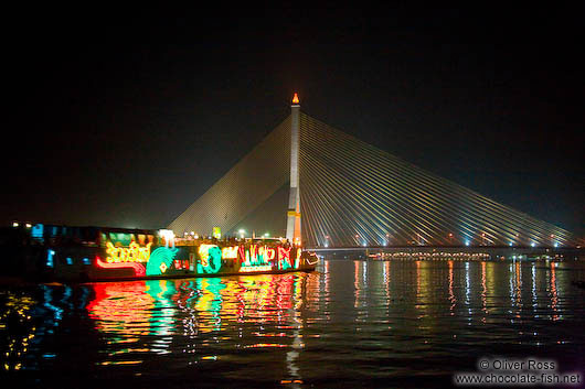 Lit tourist boat with suspension bridge across Bangkok´s Mae Nam Chao Phraya river