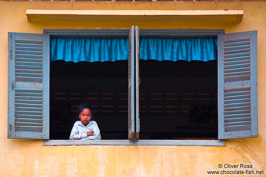 Girl looking out a window along a river near Battambang