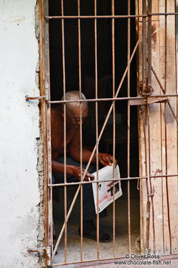 Man reading the newspaper behind bars in Havana Vieja