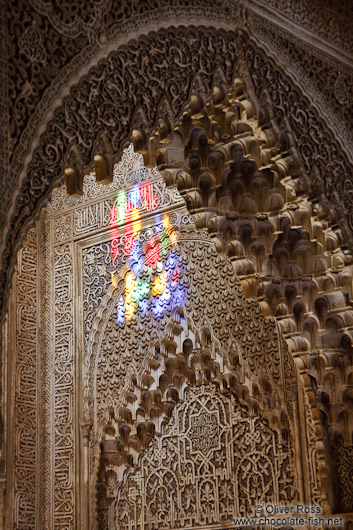 Sunlight enters through a coloured window into an ornate arabesque alcove of the Nazrin palace in the ranada Alhambra